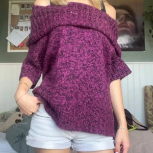 Lila offshoulder stickad tröja - Supermysig stickad tröja i melerad lila ton med bred offshoulder-krage. Tröjan har trekvartsärmar och en loose fit som ger en chill vibe. Perfekt att styla med jeans eller kjol för en trendig look.