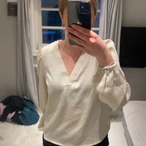 Krämvit blus med v-ringning Vero Moda - Säljer en krämvit blus från Vero Moda i storlek XS. Blusen har v-ringad hals, långa puffiga ärmar med resår vid handlederna och en lätt skimrande struktur. 