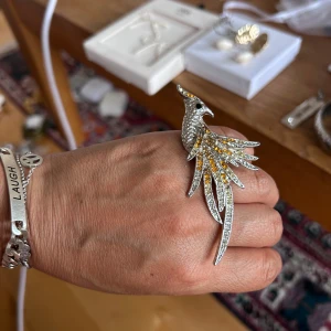 Statementring i form av fågel - Unik och iögonfallande ring i silverfärg, formad som en fågel med utsträckta vingar. Ringen är dekorerad med glittrande stenar i vitt och gult som ger en cool och lyxig känsla. Perfekt för dig som vill sticka ut och älskar detaljerade smycken.