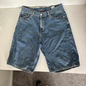 Blå jeansshorts från Sweet SKTBS - Klassiska blå jeansshorts från Sweet SKTBS med broderad logga vid fickan. Modellen är loose fit med fem fickor, bälteshällor och knappgylf. Perfekta för en chill streetwear-look och tillverkade i slitstarkt denimtyg. Använda några gånger men i princip i nyskick