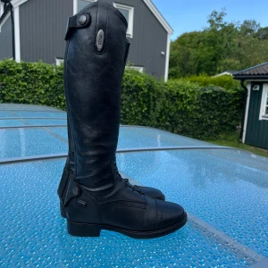 Svarta ridstövlar från CRW i skinn - Snygga svarta ridstövlar från CRW. Höga med klassisk design, snörning framtill och dekorativa sömmar vid tån. Perfekta för dig som vill ha stilrena och funktionella stövlar till ridning.