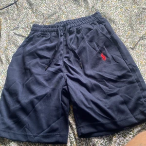 Marinblå shorts från Polo Ralph Lauren - Snygga marinblå shorts från Polo Ralph Lauren med klassisk röd broderad logga på benet. Mjukt bomullsmaterial, elastisk midja med snörning och två sidofickor. Perfekta för sommaren och chill dagar. Stilsäkra och bekväma, passar till allt.
