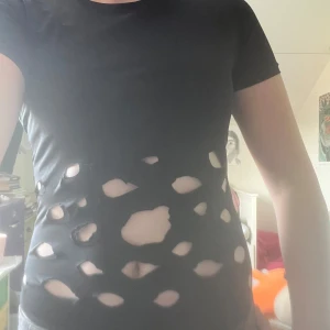 Svart body med cutouts från Pull&Bear - Svart tight body från Pull&Bear med korta ärmar och stora cutouts framtill som ger en edgy vibe. Gjord i stretchigt material som sitter snyggt mot kroppen. Perfekt för dig som vill sticka ut med en unik och cool look.