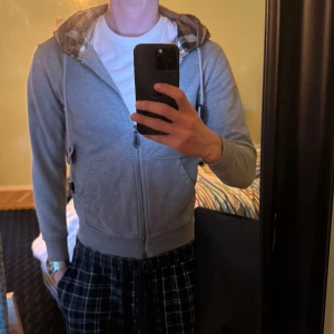 Grå hoodiejacka från Burberry - Säljer en grå zip från Burberry, har haft den i ungefär ett år. Den har blivit kort i armarna på mig. Som ni ser på sista bilden så har ”huvsnöret” lossnat lite från tvätt. Men den har alltid tvättats i tvättpåse separat så den är i fint skick förutom det med snöret. Hör gärna av er om mer frågor, mvh Gunnar 