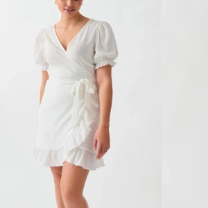 Vit omlottklänning med volang - Superfin vit kort omlottklänning med puffärmar, v-ringning och volangkant. Knytband i midjan ger en snygg siluett och tyget känns lätt och luftigt. Perfekt för sommarens alla tillfällen! Nypris 400kr, använd vid endast ett tillfälle.