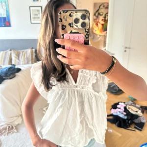 Vit blus med volang från Neo Noir❣️ - Supersöt vit blus från Neo Noir med volangdetaljer längs ärmar och axlar. Blusen har v-ringning, broderade partier och är tillverkad i ett lätt och luftigt bomullstyg. Så söt och passar till allt!😍