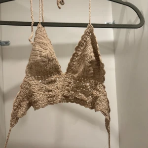 Beige virkad croppad linnetopp - Säljer en beige virkad linnetopp med knyt i nacken och ryggen. Toppen har triangelformade kupor och fina virkade detaljer längs kanterna. Köptes i Spanien! Perfekt för sommaren och ger en boho-vibe till din outfit. Liten i strl!🤎