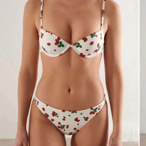 Vit bikini med jordgubbsmönster Aim'n - Superfin bikini (överdel+ underdel) från Aim'n i storlek S med vit bas och sött jordgubbsmönster i rött och grönt. Bikinin har bygel-bh med smala axelband och klassiska bikinitrosor. Materialet är stretchigt och består av polyester och spandex – perfekt för sommardagar på stranden!