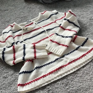Randig stickad tröja från Rut m.fl. - Vit stickad tröja från Rut m.fl. med röda och marinblå ränder. Tröjan har lång ärm, rund halsringning med snörning och ribbade muddar. Ger Pippi vibes om du gillar det🥰