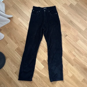 Svarta manchesterbyxor från Gina Tricot - Snygga svarta manchesterbyxor från Gina Tricot med hög midja och raka ben. Byxorna har klassisk femficksdesign, bälteshällor och silverfärgade nitar. Perfekta för dig som gillar en stilren och trendig look.