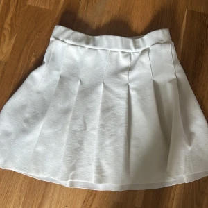 Vit plisserad kortkjol i polyester - Superfin vit kortkjol med plisserade veck och bred linning. Kjolen är gjord i ett lite strukturerat tyg av polyester och elastan som ger en snygg passform. Perfekt för en fräsch och sportig look. Och storleken står på 146 men det är bara det minsta storleken så man kan också ha storlek 152 max