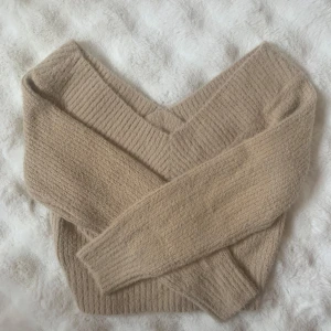 Beige stickad v-ringad tröja - Supermysig beige stickad tröja från H&M, märket Divided, med bred v-ringning som går att bära offshoulder. Tröjan har lång ärm och ribbade muddar vid ärmslut och nederkant. 