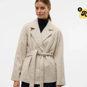 Beige kappa med bälte från Vero Moda - Stilren beige kappa från Vero Moda med bred krage och knytskärp i midjan. Jackan har en rak passform, är långärmad och tillverkad i en mjuk ullmix. Perfekt för dig som gillar en clean och klassisk look.