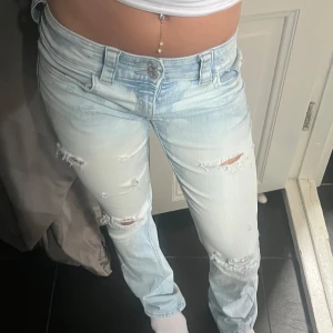 Jeans med slitningar  - Säljer ett par ljusblå jeans med slitna detaljer, dem är en bootcut design. Jeansen har låg midja, stretchigt material och snygga bakfickor med lock och knapp. Perfekta för en avslappnad och trendig look💗🌸