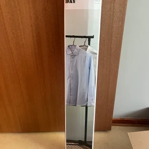 Klädhängare - En stilren ljusblå skjorta med klassisk krage och knäppning framtill. Skjortan har lång ärm och rak passform, perfekt för en clean och enkel look. Passar dig som gillar tidlös stil och vill ha något som funkar till många outfits.