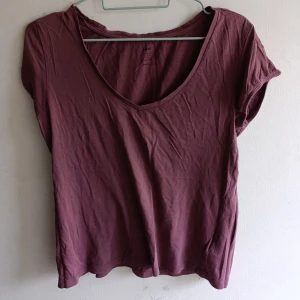 Vinröd / lila  t-shirt med v-ringning H&M - Enkel vinröd t-shirt från H&M med v-ringad hals och korta ärmar. Modellen är rak och har en avslappnad passform, perfekt till jeans eller kjol. Tillverkad i mjuk bomull som känns skön mot huden.