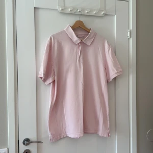 Ljusrosa pikétröja i bomull XXL - Säljer en ljusrosa pikétröja från Dressman i storlek XXL. Tröjan har klassisk krage, knäppning framtill och är tillverkad i mjuk bomull. Perfekt för dig som gillar en enkel och stilren look med korta ärmar och relaxed fit.