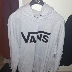 Grå hoodie från Vans XX-Large - Snygg grå hoodie från Vans i klassisk modell med stor svart logga framtill. Tröjan har huva med snörning och en stor magficka. Perfekt för dig som gillar streetwear och vill ha en chill och bekväm stil.