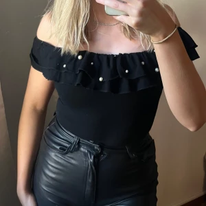 Body med volang och pärlor - Svart offshoulder body med dubbla volanger och pärldetaljer längs kanten. Använd vid ett tillfälle.💕
