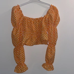 Orange blommig blus med puffärmar - Superfin orange blus med vita små blommor och puffiga långa ärmar. Croppad modell med resår vid axlar och ärmslut för en söt och trendig look. Perfekt för sommarens alla tillfällen!