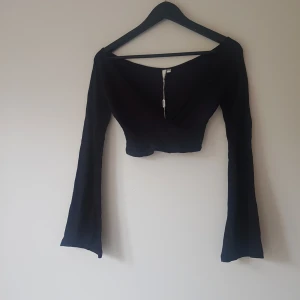 Svart croppad omlottopp NLY Trend - Snygg svart croppad omlottopp från NLY Trend med långa utsvängda ärmar och djup v-ringning. Toppen har en stilren och trendig look som passar perfekt till höga jeans eller kjol. Mjuk och stretchig känsla för en bekväm passform.  Ny med lapp så inget att anmärka på 
