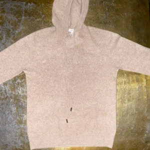 Beige hoodie i merinoull från Zantiore - Priset kan diskuteras! Mysig beige hoodie från Zantiore i kashmir. Tröjan har huva med snörning och långa ärmar. Perfekt för dig som gillar en enkel och stilren look med lyxig känsla. Passar dig som vill ha något mjukt och skönt till höst och vinter.den är syd i halsen men det är inget man ser.