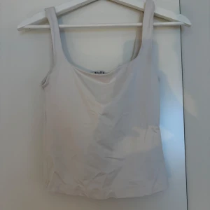 Beige linnetopp från NA-KD - Säljer en stilren beige linnetopp från NA-KD i storlek XS. Toppen har breda axelband och en klassisk, rak passform. Perfekt att matcha med jeans eller kjol för en enkel och clean look.