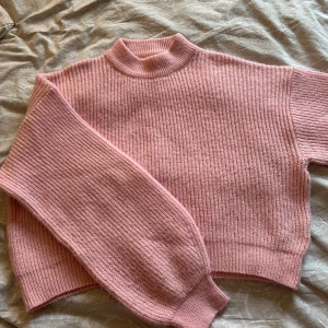 Rosa stickad tröja med hög krage - Supermysig rosa stickad tröja med ribbad struktur och hög krage. Tröjan har långa ärmar och en loose fit som ger en chill vibe. Perfekt att slänga på sig när det är kallt ute. Passar dig som gillar en enkel men söt stil.