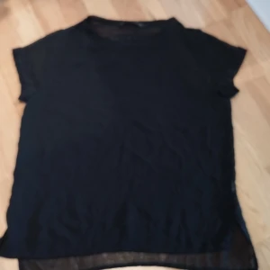 Svart topp från Zara Basic XS - Svart kortärmad topp från Zara Basic i storlek XS. Tunt, lätt material med broderad Z1975-detalj och transparent baksida Enkel och stilren design som funkar till många looks. 