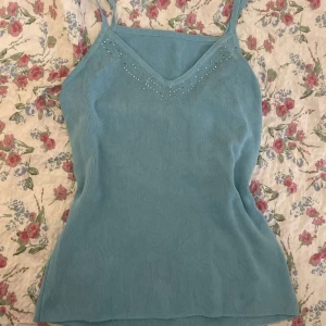 Ljusblått linne med pärlor - Supersöt ljusblå linnemed smala axelband och v-ringning framtill. Toppen har små pärldetaljer längs urringningen som ger en extra touch. Perfekt för varma dagar och enkel att styla med jeans eller kjol.