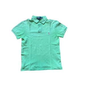 Ralph Lauren piké  - Fräsch grön pikétröja från Polo Ralph Lauren i slim fit. Klassisk krage, två knappar och broderad rosa logga på bröstet. Tillverkad i bomull och perfekt för dig som gillar stilren och sportig vibe. Jag skickar ej bild när jag bär plaggen och jag vet ej vilken längd och vikt de passar då jag inte prövar kläderna jag säljer 😃