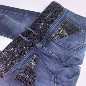 Guess Starlet Skinny jeans med paljetter - Mörkblå skinny jeans från Guess, modell Starlet Skinny. Jeansen har snygga svarta paljett-detaljer på fickor och linning som ger extra bling. Klassisk femficksmodell i stretchig denim med låg midja och smal passform. Perfekta för dig som vill sticka ut lite extra.