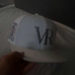  Vonroe Collective 55,8cm - Snygg vit keps från Vonroe Collective med broderad VR-logga framtill och detaljerad brodyr på sidan med palmer och text. Kepsen har rak skärm och klassisk passform. Perfekt för dig som gillar streetwear och vill sticka ut med stilrena detaljer.