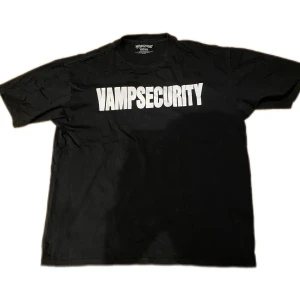 VAMPSECURITY Playboi Carti Merch - Svart t-shirt från Maggot med stor vit VAMPSECURITY-print över bröstet. Klassisk rund halsringning och korta ärmar. Tillverkad i mjuk bomull, perfekt för dig som gillar statement-plagg och streetwear-vibe.