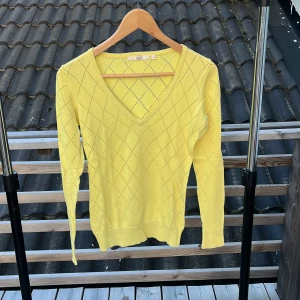 Gul v-ringad tröja från Riley - Gul långärmad tröja från Riley med v-ringning och diskret rutmönster. Tröjan är i mjuk bomull och har en slim passform som sitter snyggt. Perfekt för dig som gillar färg och vill sticka ut lite extra.