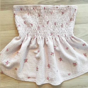 söt ljusrosa smock topp - i jättefint skick och inga defekter alls😊. Har avtagbara band så den blir en tube topp annars har den söta band med blommor på! (Se bilder). Säljs inte längre online💗