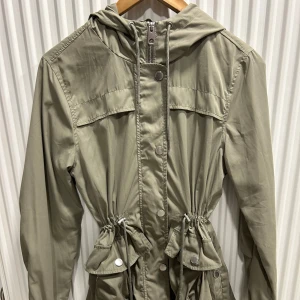 Militärgrön parkajacka med huva och snörning - Militärgrön vår/höstjacka med huva, dragkedja, tryckknappar framtill, snörning och fickor. Storlek XS men passar även S. 75kr💚🌾🍂