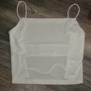 Vit bandeau tubtopp med tunna band - Säljer en stilren vit bandeau tubtopp med tunna axelband. Toppen har en enkel och clean design framtill och coola öppna detaljer baktill med tre horisontella band. Jättesnygg, dock för liten på mig