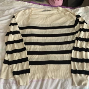 Randig stickad tröja från Zara - Snygg stickad tröja från Zara i vitt med svarta horisontella ränder. Tröjan har lång ärm, ribbade muddar och en liten slits vid ärmslutet för extra detalj. Perfekt för dig som gillar en klassisk men trendig look.