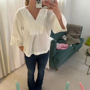 Vit blus med v-ringning och spets - Superfin vit blus i luftig bomull med v-ringning och spetsdetaljer samt små bollar längs halsringningen. Vida trekvartsärmar med dekorativa sömmar. Otroligt fin till sommaren🤍🤍Använd enstaka gång 