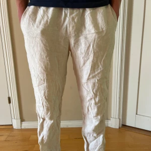 Beiga linnebyxor med rak passform - Snygga och luftiga beiga linnebyxor med rak passform och sidfickor. Perfekta för varma dagar och ger en avslappnad men stilren look. Byxorna har en enkel design utan synliga detaljer och är tillverkade i ett svalt linnematerial.