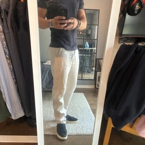 Beiga linnebyxor med rak passform - Säljer ett par snygga beiga linnebyxor med rak passform och klassisk midja. Byxorna har dragkedja framtill och sidfickor, perfekta för en chill och stilren look. Lätta och luftiga, passar grymt till sommaren.