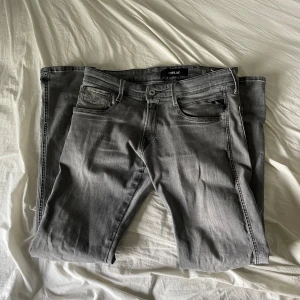 Replay grå jeans slim fit - Snygga grå jeans från Replay i modellen Anbass. Jeansen har en slim fit passform, klassisk femficksdesign och diskreta detaljer på bakfickorna. Tillverkade i mjukt jeansmaterial med lite stretch för extra komfort.