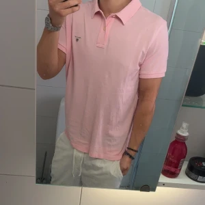 Ljusrosa pikétröja från GANT - Säljer en ljusrosa pikétröja från GANT med klassisk krage och två knappar framtill. Tröjan har GANT-logga broderad på bröstet och är tillverkad i mjuk bomull. Perfekt för en clean och fräsch stil under vår och sommar.