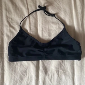 Svart bikiniöverdel från KappAhl - En stilren svart bikiniöverdel från KappAhl i sportig modell med smala axelband som knyts i nacken. Mjuk och följsam passform, perfekt för strand eller pool. Tillverkad i ett snabbtorkande syntetmaterial.
