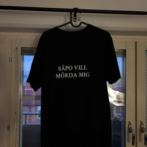 Svart t-shirt(säpo vill m*rda mig) - Svart t-shirt med vit text på bröstet där det står 'SÄPO VILL MÖRDA MIG'. Klassisk passform med rund hals och korta ärmar. Perfekt statement-plagg för dig som vill sticka ut. Materialet är bomull.