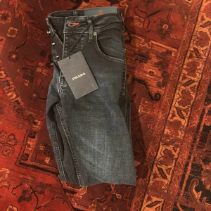 Prada jeans - Snygga svarta jeans från Prada med klassisk femficksdesign och silverfärgade knappar. Jeansen har en diskret tvättad look, raka ben och en röd detalj vid knapphålet. Tillverkade i mjukt denimtyg för en bekväm känsla. Aldrig använd