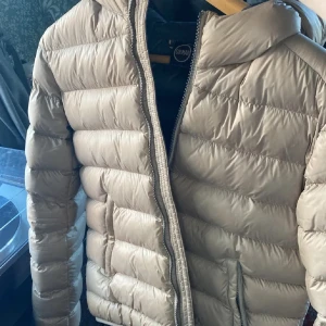 Beige Colmar pufferjacka med huva - Säljer min jacka från Colmar som såklart är äkta, inga defekter och den är jättefin, fått väldigt många komplimanger men behöver tyvärr sälja för jag köpt en ny. pris kan diskuteras. den är i italiensk storlek 46 vilket motsvarar S  