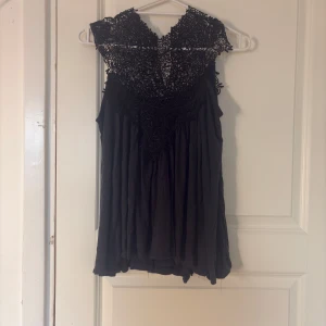 Svart blus med spets från Lise Sandahl - Supersnygg svart blus från Lise Sandahl med detaljerad spets upptill och lös flowy passform. Blusen är ärmlös och har en romantisk känsla med vackert mönstrad spets över axlar och bröst. Perfekt för dig som gillar unika detaljer och stilren look🌸