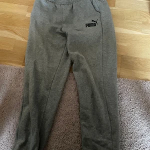 Grå mjukisbyxor från Puma - Säljer ett par grå mjukisbyxor från Puma med elastisk midja och logga på vänster lår. Perfekta för chill dagar eller när du vill vara bekväm. Klassisk passform och mjukt material.